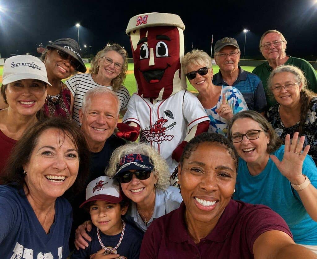Security First Asset Management clients and staff gather for a group photo with the Macon Bacon mascot on the field at Luther Williams Field.