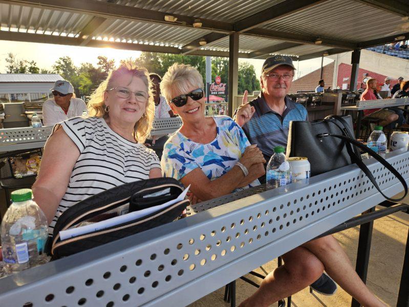 Three guests smile at their table in the group seating area as the sun sets over the ballpark.
